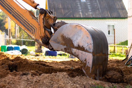An excavator metal bucket digs sand or clay on a construction site, digging a trench.の写真素材