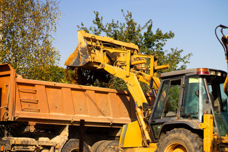 A wide metal excavator bucket digs sand or clay, loading it into a dump truck at a construction site.の写真素材