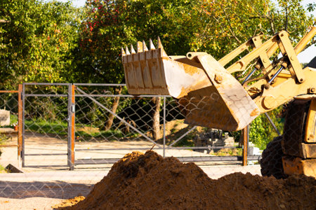 A wide metal excavator bucket digs sand or clay, loading it into a dump truck at a construction site.の写真素材