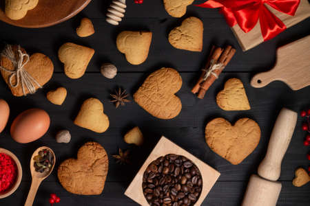 Gingerbread heart shaped cookies, spices, coffee beans and baking supplies on black wood backgroundの写真素材