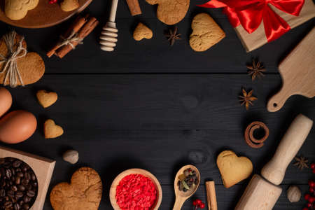 Gingerbread heart shaped cookies, spices, coffee beans and baking supplies on black wood background, copy spaceの写真素材