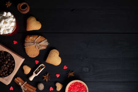Gingerbread heart shaped cookies, spices, coffee beans and baking supplies on black wood background, copy spaceの写真素材