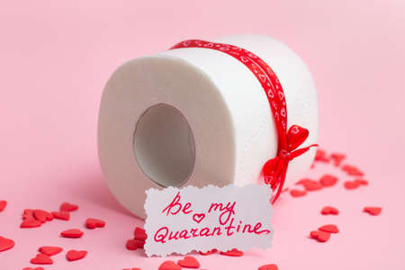 Roll of toilet paper as Valentine's Day gift with note Be My Quarantine, next to red hearts on pink backgroundの写真素材