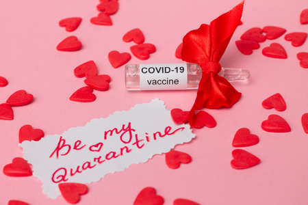 Ampoule with COVID-19 vaccine as gift for Valentine's Day with note Be My Quarantine, next to red hearts on pink backgroundの写真素材
