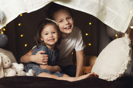 Siblings in a hut of chairs and blankets. Brother and sister laugh and play at homeの写真素材