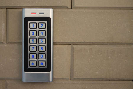 Silver intercom call panel with blue number buttons, on a brick beige fence pillar of a private...