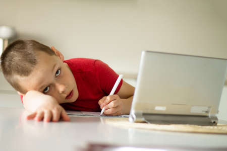 Boy 6-10 completes school homework online in the kitchen, looking at the tablet computer. Distant...