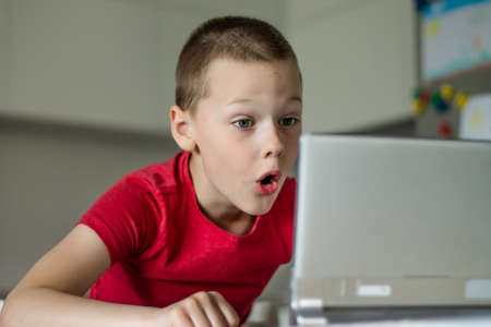 Boy 6-10 completes school lessons and homework online in the kitchen, looking at the tablet...