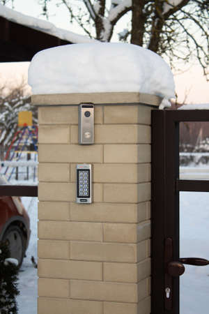 Silver intercom call panel with blue number buttons and a video camera, on a brick beige fence pillar of a private house. Verticalの写真素材