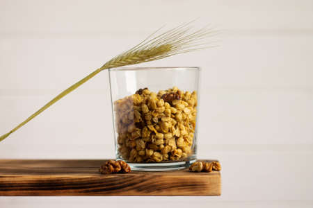 Cereal granola in a transparent glass with rye spike and walnuts on a shelf on a white background. Copy space.の写真素材