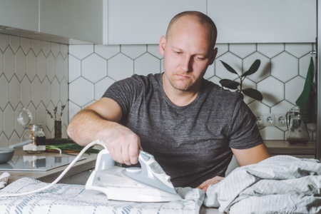 Serious man irons bed linen. Father is engaged in household chores.の写真素材