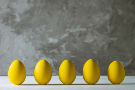 Row of five bright yellow Easter eggs, standing on white wooden surface on gray concrete background, copy spaceの写真素材