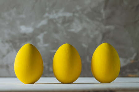 Row of five bright yellow Easter eggs, standing on white wooden surface on gray concrete background, copy spaceの写真素材