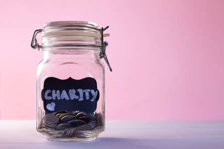 Glass jar with coins with chalk tag Charity on a pink background, donation and charity concept. Copy space.の写真素材