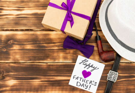 Greeting card Happy Father's Day with a gift box and men's accessories on a rustic wooden tabletop....