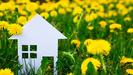 White silhouette of a toy house cut out of cardboard on a background of dandelions. A small house made of white paper. Copy spaceの写真素材