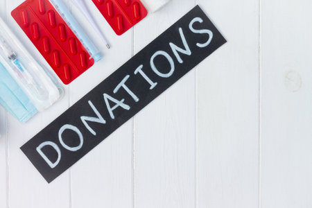 Medications, masks, gloves, syringes, thermometer with a chalk Donations sign on a white wooden table. Flat lay. Copy space. Charity and donation concept.の写真素材