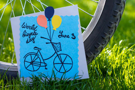 Handmade colored paper greeting card next to a bicycle wheel on grass background. DIY. World bicycle dayの写真素材
