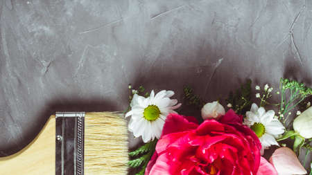 Brush that paints with flowers instead of paint on gray concrete background. Large tulip, roses and...