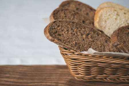 Partially blurred wicker basket with black and white bread on white tablecloth, on wooden table