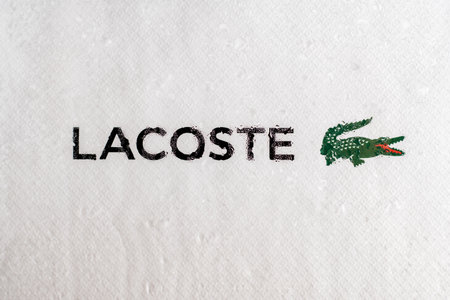 Minsk, Belarus 05/07/2021: Lacoste logo and name behind glass on white background with water drops.