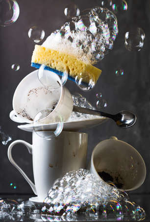 Stack of dirty white dishes on dark background, with washing sponge and bubblesの写真素材