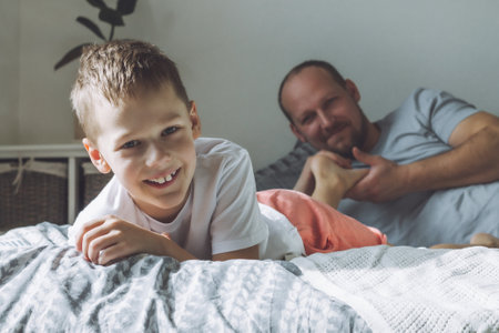 Father plays with his son 7-10 on bed. Dad tickles kids feet. Family having funの写真素材