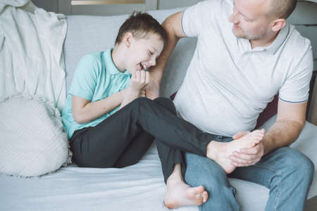 Father plays with his son 7-10 sitting on couch. Dad tickles kids feet. Family having funの写真素材