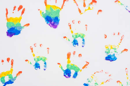Child handprints of rainbow colors on white sheet of paper. Top viewの写真素材