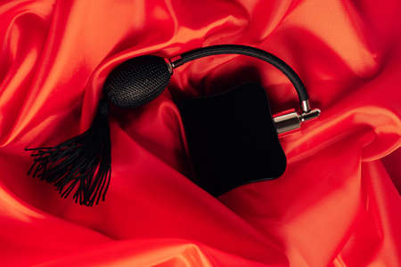 Black bottle of eau de toilette or perfume with long tassel spray pomp lies on red background of...