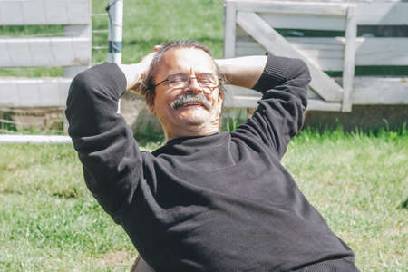 Portrait of gray-haired adult mature man with glasses and mustache sitting on beanbag and smiling...