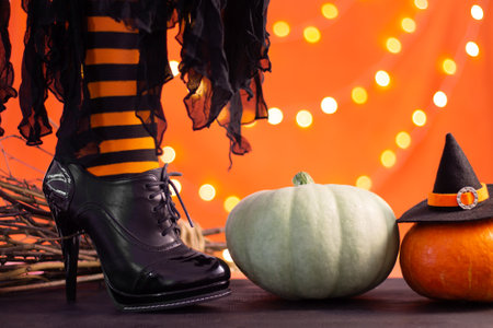 Witch legs in striped stockings and high heel shoes with Halloween pumpkins on an orange background with bokeh. Copy space.の写真素材