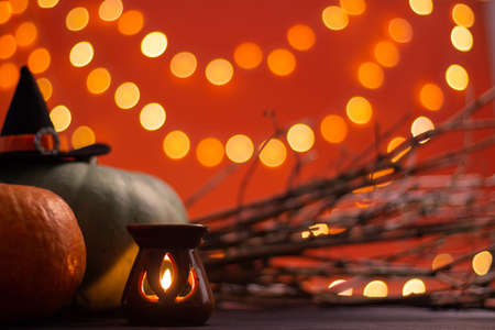 Hat of a witch with branches, candle and Halloween pumpkins on an orange background with bokeh. Copy space.の写真素材