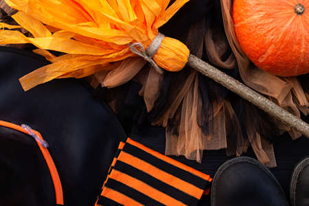 Orange and black Halloween flatlay. Witch clothes: stockings, boots, hat, broom, skirt on black backgroundの写真素材