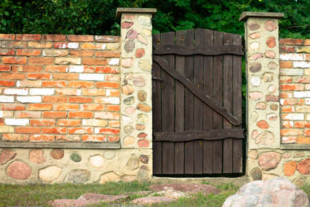 Landscaping. Red brick fence with brown wooden gate in the courtyard of private house, stone path.