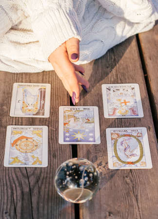 Woman's hand with purple nails points to five Tarot cards spread out on wooden surface next to crystal ball. Vertical. Minsk, Belarus - 07.28.2021のeditorial素材