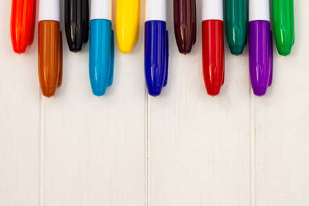 Multi-colored markers on a white wooden background. Top view. Copy space