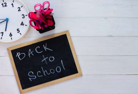 Back to school black chalk board on a white wooden background, pink supplies. Top view. Copy space. Education concept.の写真素材