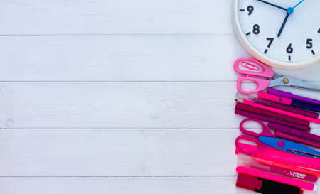 Pink school supplies and clock on a white wooden background. Top view. Copy space. Education and...