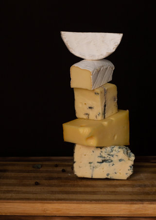 Different types of cheese on a rustic wooden cutting board on a dark background. Vertical. Copy...