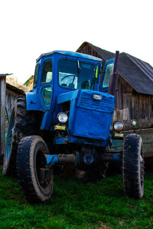 Old vintage blue rusty tractor on the background of farm buildings. Sowing work in the fieldの写真素材