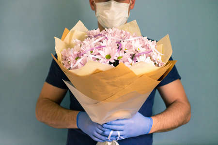 courier in medical gloves and a mask delivers a bouquet of chrysanthemums. Contactless flower...