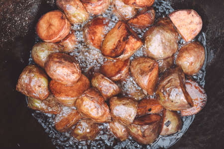 Baked potatoes cooked in yard cauldron with firewood burning in it with lots of boiling sunflower oilの写真素材