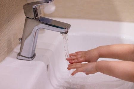 Child washes hands. Little girl washes her hands with soap under a faucet with flowing water. Close...