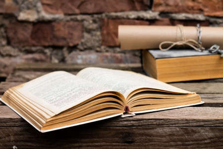 Old books with a scroll and key on a rustic wooden surface on a brick wall backgroundの写真素材