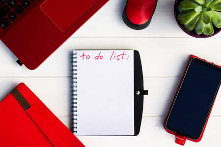 Notebook with To Do List with phone, red diary and laptop on a white wooden background. Top view. Copy spaceの写真素材