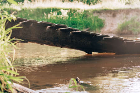 Skewed crooked wooden bridge over small river made of old planks