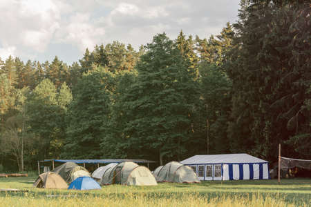Tent town against backdrop of forest on meadow with pavilion and volleyball net. Camping conceptの写真素材