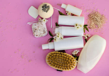 White cosmetic bottles, bath bomb, handmade soap, bath salt, massage brush, sponge, cotton buds with cherry flowers on a pink background. Natural organic cosmetics concept.の写真素材