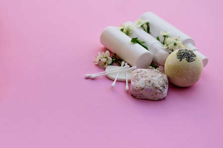 White cosmetic bottles, bath bomb, handmade soap, bath salt, massage brush, sponge, cotton buds with cherry flowers on a pink background. Natural organic cosmetics concept.の写真素材
